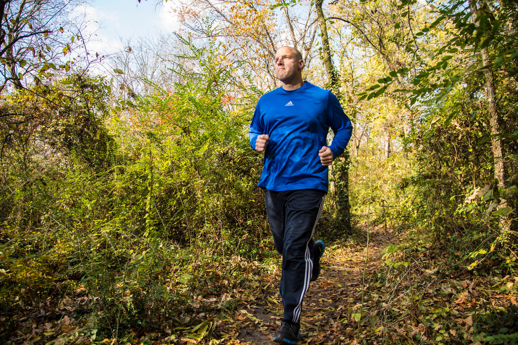 Man running on a trail in a forest wearing a concealed holster in fitness clothing.