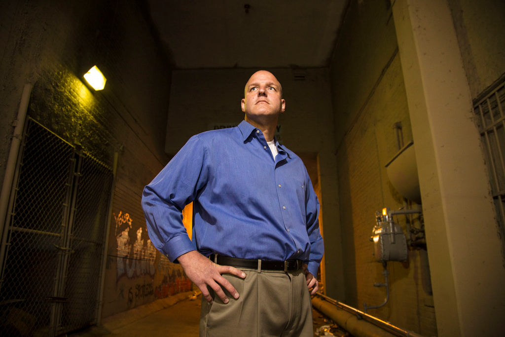Man in a blue shirt standing in an industrial setting with a light fixture above.