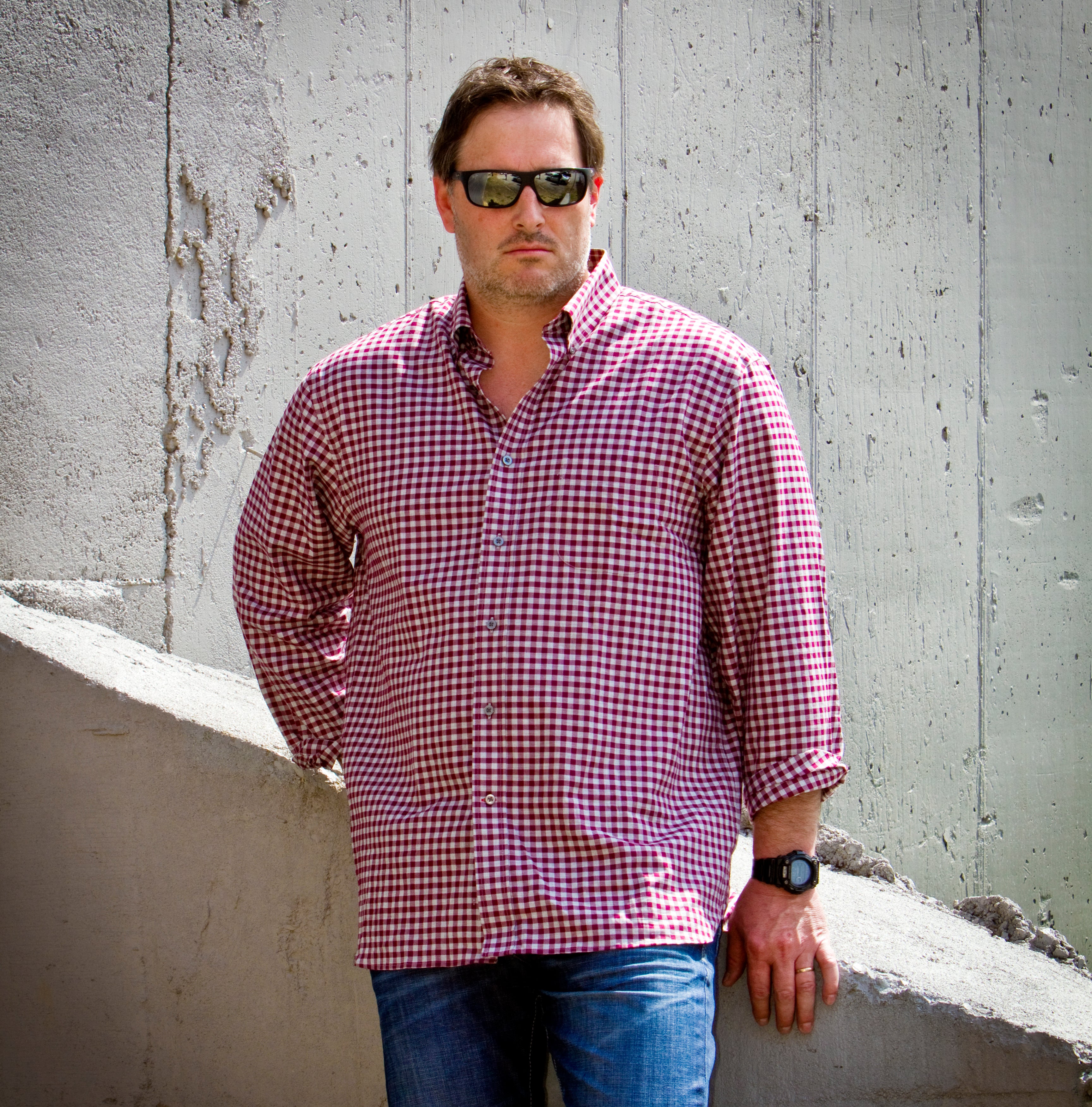Man wearing a red and white checkered shirt against a concrete wall.