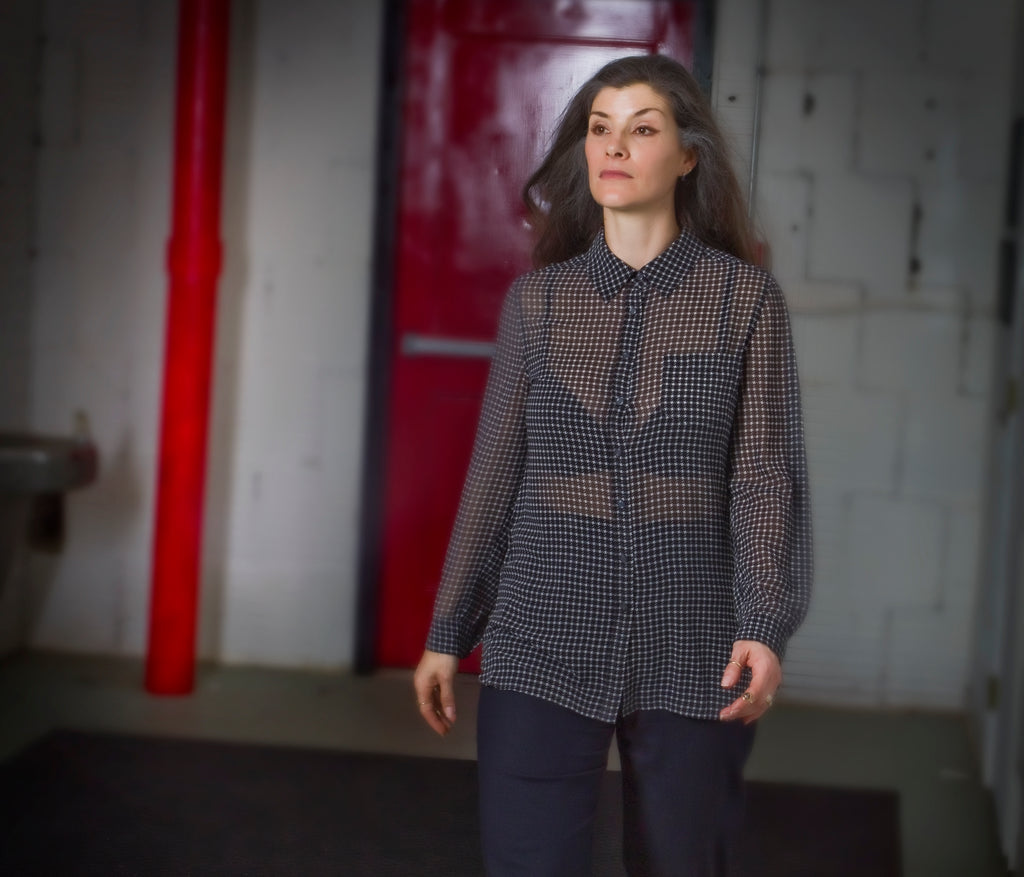 Woman wearing a checkered shirt in an industrial setting with red pipes and white walls carrying concealed firearm