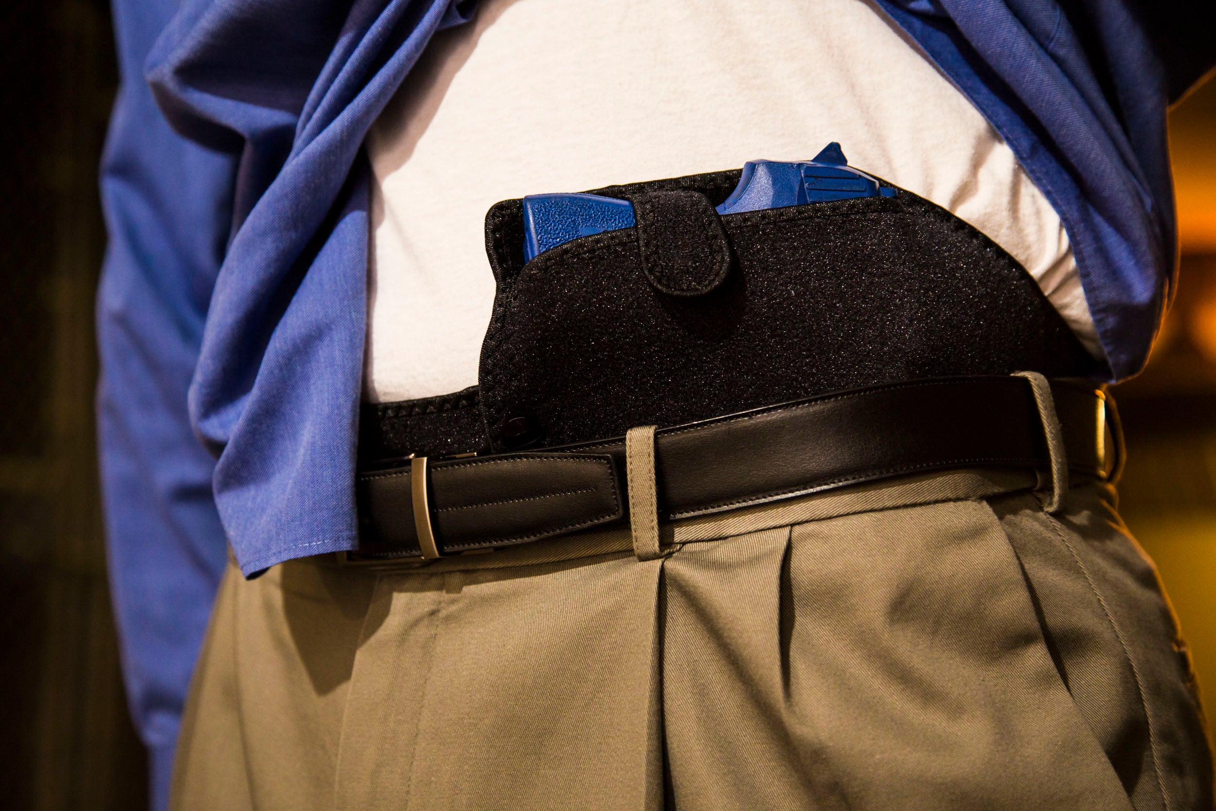 Person wearing a black holster with blue accents on a white shirt and beige pants.