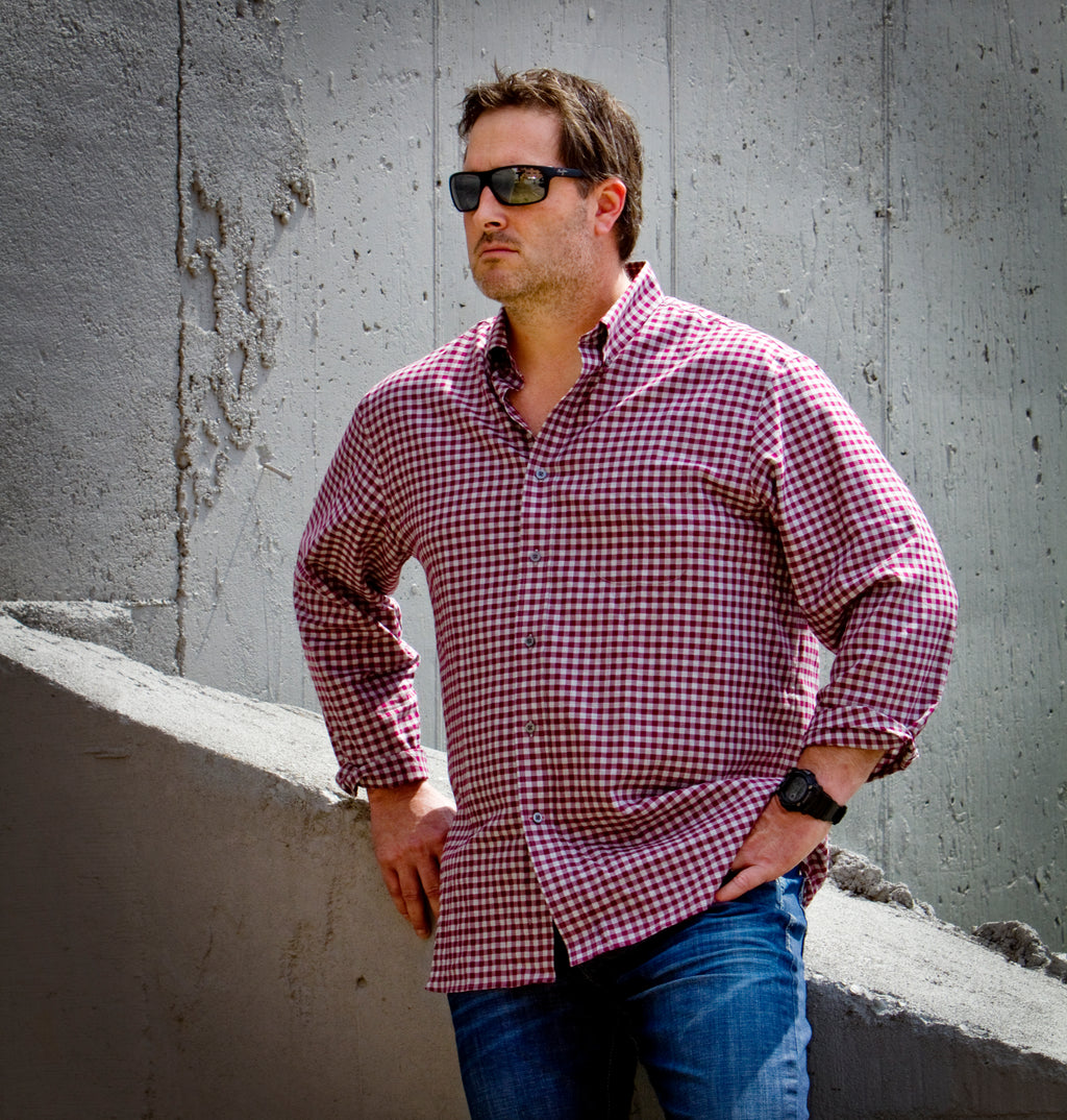 Man wearing a red plaid shirt and sunglasses against a concrete wall.