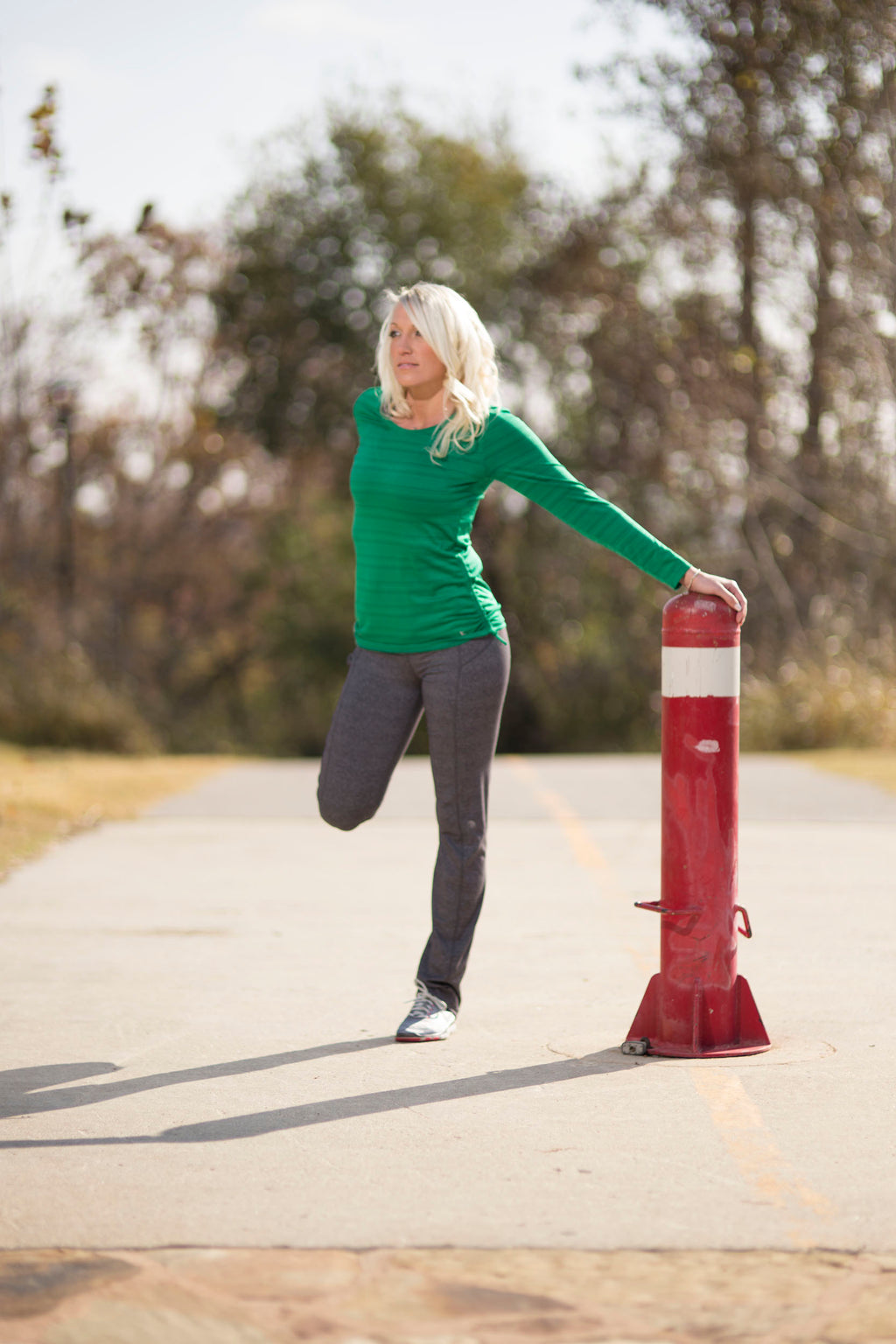 Woman in green shirt and gray pants standing next to a red and white fire hydrant wearing concealed holster for fitness